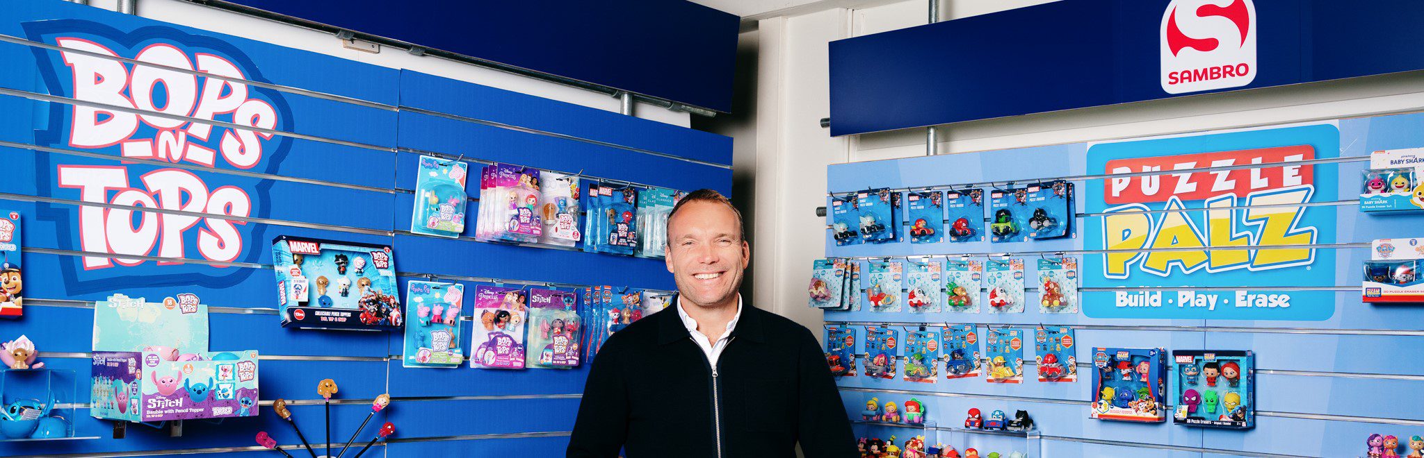 This is an image of Hein, standing in front of some of Sambro's own brand products, Puzzle Palz and Bops n Tops.
